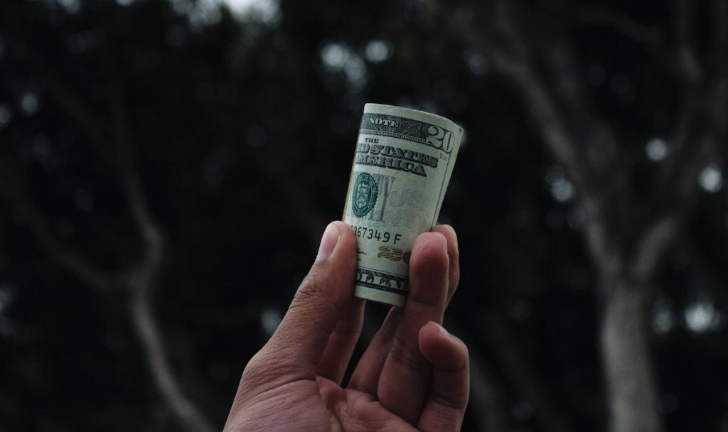 Hand holding roll of money to symbolize a business owner paying his helpers what they are worth.